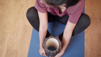 Top view Asian woman doing leg stretching on floor exercise mat in her apartment living room, sport equipment foam roller, hamstring glutes therapy rehabilitation, health rehab routine flexibility video