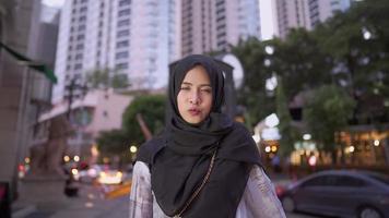 Gut aussehende junge erwachsene muslimische Frau lächelt in die Kamera und zeigt ein gutes Leben in der Stadt, moderne Lifestyle-Religion, traditionelle Hijab-Kulturen, Hochhäuser mit Eigentumswohnungen im Hintergrund video