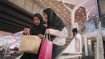 Two muslim ladies wear traditional hijab walking down shopping mall stairs holding shopping bags, buying clothes goods, arab wealthy society, credit card points redemptions, sales discount promotion video