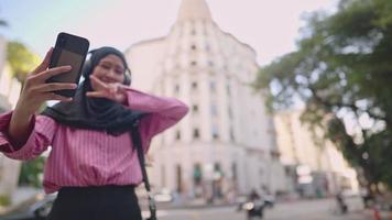 Junge asiatische muslimische Touristin im Hijab, die sich selbst mit einem schönen Wahrzeichen auf Hintergrund, Lebensstil und Reisen selfies macht, Geschichten teilt, postet auf der Zeitachse, neuer Feed, glückliches und fröhliches Mädchen video