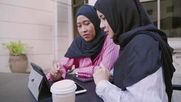 attraente asiatico musulmano amico d'insegnamento femminile che impara nuove abilità, spiegando sull'uso della penna wireless e della tavoletta digitale, team di progettazione che lavora insieme al moderno tavolo da caffè all'aperto