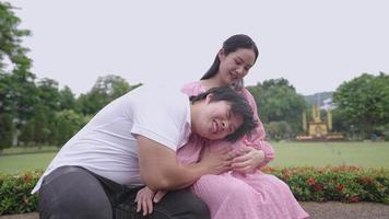 Young asian couple feel happy with their first child of the family, father listening and talking with his baby inside pregnancy tummy, young expectant mother and husband sit down relaxing in the park video