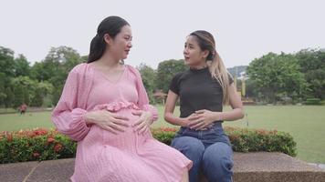 giovane donna incinta asiatica che ha una conversazione utile con la sua ragazza seduta nel parco all'aperto, società del femminismo, consulenza sulla gravidanza femminile, riunirsi per alleviare lo stress, parlare felicemente positivo video