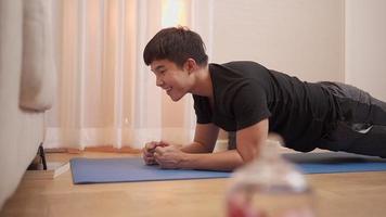 jeune homme asiatique planquant et regardant un smartphone en même temps, exercice pendant le verrouillage du covid-19, entraînement à domicile faisant de l'exercice de loisirs et de passe-temps, concept de bien-être heureux, divertissement d'entraînement à domicile video