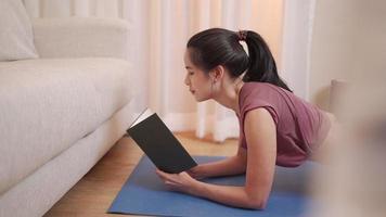asiatisk ung kvinna som plankar och läser samtidigt, tränar under covid-19-låsning, hemmaträning tränar i vardagsrum med soffa, hemutbildning collegestudent genomgång studieanteckning föreläsning video