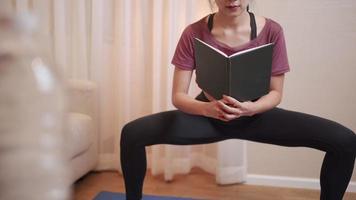 mujer joven asiática que hace yoga y lee al mismo tiempo, hace ejercicio, bloquea el covid, hace ejercicio en casa, hace ejercicio en la sala de estar, estudia educación a distancia. bienestar humano, dama independiente multitarea video