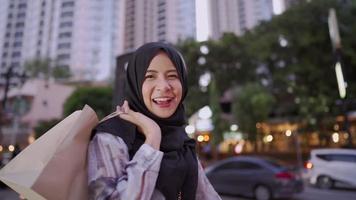 Young Asian muslim feel happy showing shopping bags to camera, standing on the street, capitalist consumer spending money, discounts sales products, enjoy shopping at the mall, downtown city lifestyle video