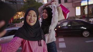 jovem amiga de meninas muçulmanas asiáticas tirando selfies em pé na rua gosta de viajar para fazer compras gastar dinheiro em pé no lado da estrada urbana com carros passando no fundo, vida moderna de mídia social