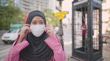 ung asiatisk muslimsk kvinna ta bort ansiktsmask. förtroende social distansering stående på vägkorsningen, stad urban ny normal, isolerad hålla sig borta, covid-19-pandemi, skydd mot infektionssjukdomar video