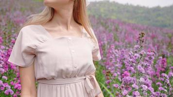 una chica de cabello rubio despreocupada bailando lentamente dentro de un floreciente campo de flores púrpura, una joven atractiva que se siente libre dando vueltas en el jardín de primavera en el día de verano, una mujer tocando la naturaleza, cuidado del cuerpo video