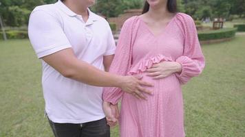 Happy young couple of expectant parents, a pregnant woman and her husband strolling together with holding hands and touch at mother's stomach, counting down for baby, relaxing pregnancy exercise video