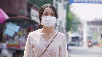 framifrån av en blandras kvinna med mörkt hår som promenerar på de tysta utomhusmarknadsgatorna under epidemin, bär en ansiktsmask mot luftföroreningar och covid19, nödvändiga livsfaktorer video