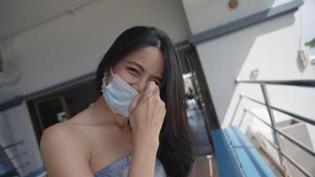 Closeup a beautiful asian woman in blue casual strapless shirt smiling to camera with slowly wearing a medical against Coronavirus pandemic, a respiratory system protection when outside, health care video