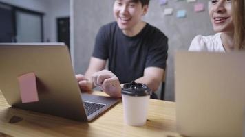 joven autónomo asiático trabajando juntos en la discusión de proyectos grupales con una lluvia de ideas usando una computadora portátil inalámbrica en el espacio de trabajo de la oficina en casa, reunión de trabajo en equipo, modelos sonrientes de emociones positivas video