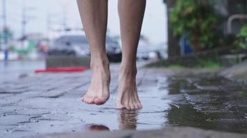 Close up light skin asian girl barefoot stomp and playing on  puddles on the raining day, wet and humid tropical weather in asia, street side area, fun time splashing water, jumping goofy around video