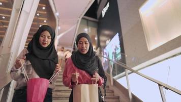 una mujer musulmana multiétnica que pasa tiempo de calidad juntos comprando en el distrito del centro, caminando por un moderno día de compras de escaleras decorativas de hormigón, una bolsa reciclable para salvar el planeta, ángulo bajo