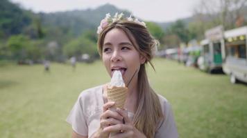 mujer rubia joven asiática comiendo helado pasando un rato feliz con un postre dulce frío mientras se encuentra dentro del campo de hierba del festival de verano, concepto de diente dulce, retrato femenino de cerca, luz solar natural