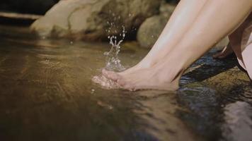 Close up female soaking her feet in the canal river stream, using hands playing with water resting freshness from nature, natural resources, feel relieve and relax, scooping natural water freshness video