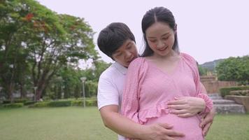 junge asiatische paare fühlen sich glücklich und warm machen sich bereit, ein neugeborenes baby zu treffen, schwangerschaftsvorbereitung, junge eltern verbringen zeit im park, ehemann umarmt und kuschelt mit schwangerer frau, familienliebe