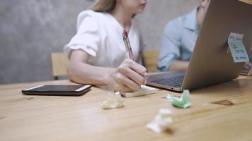 Young adult female using hand writing with pen taking note during doing group project working discussion brainstorming using wireless computer laptop at home office, busy hour working, multitask woman video