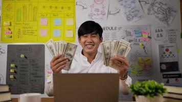 retrato de un joven hombre de negocios asiático rico disfruta de la lluvia de dinero mientras trabaja en el cargo. un hombre de negocios exitoso obtuvo un bono especial tirando dinero como un hombre de negocios loco. video