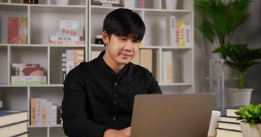 portret close-up van Aziatische zakenman die op laptop werkt en zich uitstrekt op kantoor aan huis. jonge freelancer man computer notebook te typen terwijl hij aan een bureau thuis zit. sociaal afstandsconcept. video