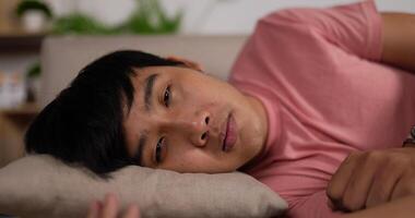 Close up portrait of Asian young man napping on sofa in living room at home. Tired man sleeping on couch. Guy relaxing looking at camera and closing eyes. video