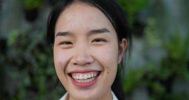 Close up face of Happy Asian female gardener owner smiling and looking at camera in the garden. Home greenery, selling online and hobby concept.