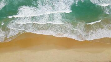 vista aérea de la playa de arena y la textura de la superficie del agua. olas espumosas con cielo. vuelo de drones de una hermosa playa tropical. increíble costa de arena con olas de mar blanco. concepto de naturaleza, paisaje marino y verano. video