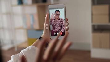 cierra la mano de una mujer feliz sosteniendo un teléfono móvil y chateando por skype con el padre. joven asiática que tiene una videollamada a través de un teléfono inteligente hablando con la familia. Internet y tecnología en línea. video