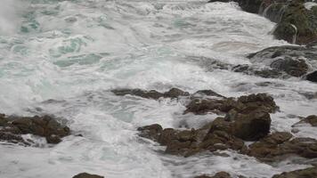 cerca de las olas del mar chocan contra las rocas de la costa creando una explosión de agua. hermosa playa tropical. increíble costa de arena con olas de mar blanco. concepto de naturaleza, paisaje marino y verano. video