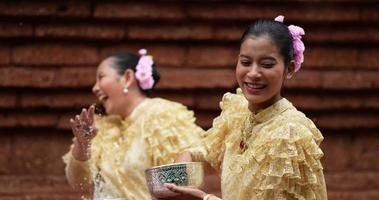 Handaufnahme, selektiver Fokus, junge schöne Frauen mit traditioneller thailändischer Tracht genießen es, Wasser im Tempel auf dem Songkran-Festival zu spritzen. thailändisches neujahr, thailändische kultur mit wasserfest