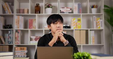 Portrait of Asian freelancer man working in front of laptop and having an idea for solving a problem. Young businessman sitting at workplace desk, being happy for getting job done. video