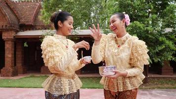 tiro de mão, duas belas mulheres com traje tradicional tailandês gostam de espirrar água no templo no festival songkran. ano novo tailandês, cultura tailandesa com festival de água