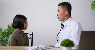 professionell asiatisk manlig läkare barnläkare med stetoskop lyssna på hjärtat av glad frisk liten flicka på kliniken. manlig läkare undersöker barn. hälso-, försäkrings- och medicinkoncept. video