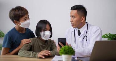 El médico pediatra asiático con bata blanca describe el estado del paciente viéndolo por teléfono en la clínica. concepto de atención médica, seguros y medicamentos. video