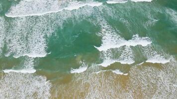 vista aérea de la playa de arena y la textura de la superficie del agua. olas espumosas con cielo. vuelo de drones de una hermosa playa tropical. increíble costa de arena con olas de mar blanco. concepto de naturaleza, paisaje marino y verano. video