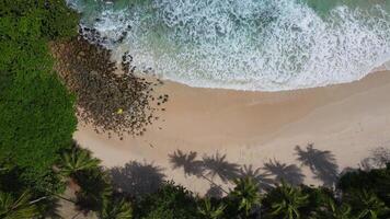 vista aérea de la playa de arena y la textura de la superficie del agua. olas espumosas con cielo. vuelo de drones de una hermosa playa tropical. increíble costa de arena con olas de mar blanco. concepto de naturaleza, paisaje marino y verano. video