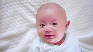 glückliche familie, süßes asiatisches neugeborenes baby, das auf einem weißen bett liegt, blick in die kamera mit einem lachenden lächeln, einem glücklichen gesicht. kleines unschuldiges neugeborenes entzückendes kind am ersten lebenstag. Muttertagskonzept.