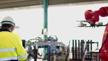 engenheiro mecânico, trabalhador técnico vestindo uniforme, capacete de segurança usando computador tablet máquina de braço robótico automatizado de controle de verificação na fábrica. conceito de indústria de fabricação automática. video