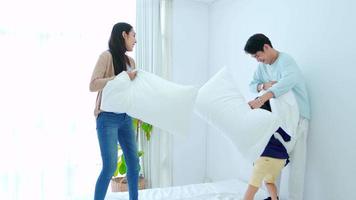 Happy family time, Young asian mother and father are playing fight pillow together with son on bed in bedroom with happy, laughing smile. Weekend parent time with love child, good time relax at home. video
