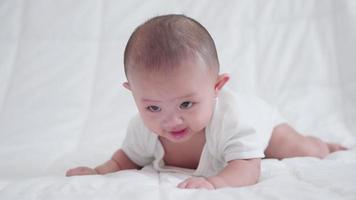 glückliche familie, süßes asiatisches neugeborenes baby, das auf einem weißen bett liegt, blick in die kamera mit einem lachenden lächeln, einem glücklichen gesicht. kleines unschuldiges neugeborenes entzückendes kind am ersten lebenstag. Muttertagskonzept. video