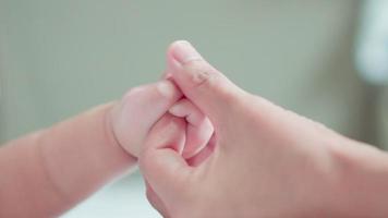 gros plan de la main mignonne du bébé nouveau-né câliner le doigt de la mère. maman utilise le doigt du pouce pour jouer, toucher la peau tendre de bébé avec amour. famille heureuse, petit nouveau bébé innocent adorable. notion de fête des mères. video