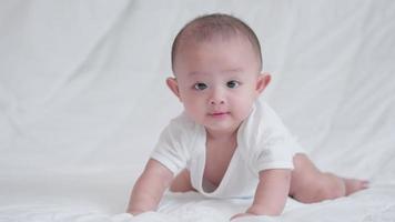 familia feliz, lindo bebé asiático recién nacido acostado jugar en la cama blanca mira la cámara con una sonrisa sonriente cara feliz. pequeño inocente nuevo bebé adorable niño en el primer día de vida. concepto del día de la madre. video