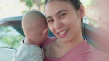 Aufnahme einer asiatischen Mutter, die mit einem neugeborenen Baby lächelt, das zusammen ein Selfie oder ein Videoanruf-Handy mit dem Vater oder den Verwandten zu Hause macht. glückliche Familienzeit. Technologie, Lifestyle-Elternschaftskonzept. video