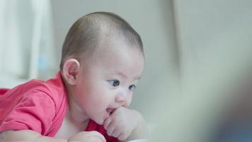 glückliche familie, süßes asiatisches neugeborenes baby trägt ein rotes hemd, das auf einem weißen bett mit einem lachenden lächeln, einem glücklichen gesicht spielt. kleines unschuldiges neugeborenes entzückendes kind am ersten lebenstag. Muttertagskonzept. video