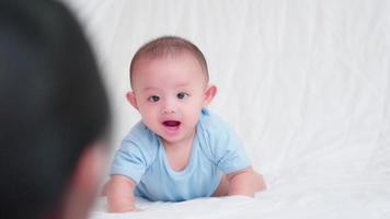 lycklig familj, söt asiatisk nyfödd baby liggande lek, kryper på vit säng och tittar på mamma. le glad ansikte medan mamma leker ta hand med kärlek. oskyldig liten pojke bedårande. mors dag koncept. video