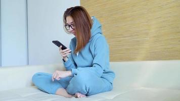 une femme au visage sérieux est allongée sur le canapé et lit des messages à l'aide d'un smartphone