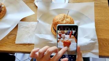 oman making photo of burger in restaurant with smartphone video