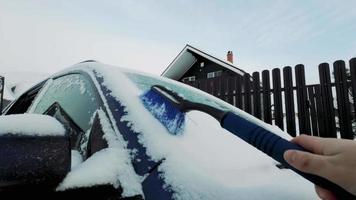 hombre limpiando el auto con el cepillo en invierno después de la nevada en la mañana. Imágenes en cámara lenta de 4k video